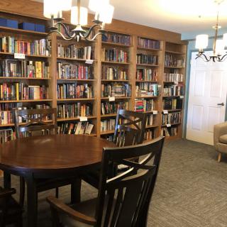 A cozy library room with wooden bookshelves filled with books, a table, and chairs for reading.