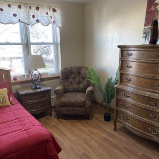 A cozy bedroom with a red bedspread, a brown armchair, and a wooden dresser.