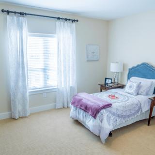 A bright and cozy bedroom with a single bed, nightstand, and window with translucent curtains.