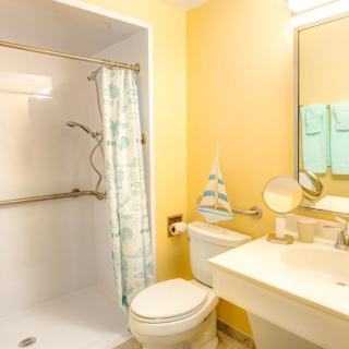 A clean and bright bathroom with a shower, toilet, sink, and mirror.