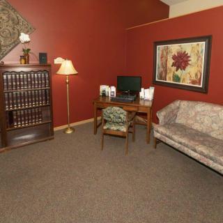 A cozy office space with a bookshelf, desk, lamp, and sofa set against red walls.