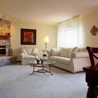 A cozy living room with a beige sofa and armchair, a glass coffee table, and a lamp, complemented by warm lighting.