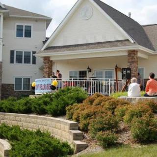 A small gathering of people at an event outside a building with a banner and landscaped surroundings.