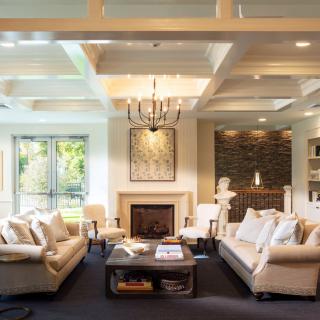 A modern and cozy living room featuring a fireplace, elegant chandelier, and comfortable seating arrangements with large windows providing ample natural light.