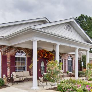A charming brick house featuring a porch with columns, surrounded by well-maintained landscaping and flower arrangements.