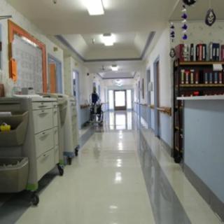 A quiet hospital corridor with medical carts and doors leading to various rooms.