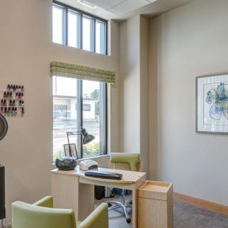 A modern office space with a desk and chairs, featuring large windows and wall art.