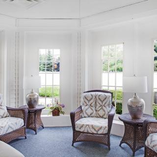 A bright living room with wicker armchairs and side tables adorned with decorative vases, set against white walls and large windows.
