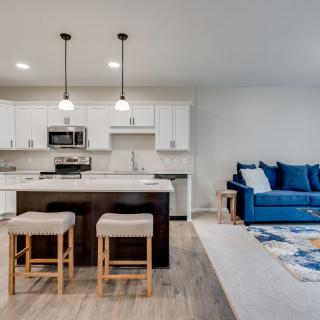 A modern open-concept kitchen and living room with an island counter, pendant lights, and a blue sofa.