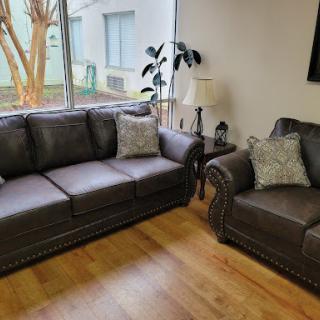 A cozy living room setup featuring a dark gray sofa and armchair, complemented by decorative pillows and natural light coming through the windows.