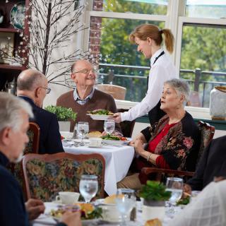 A group of people dining together in a restaurant with a waitress serving food.