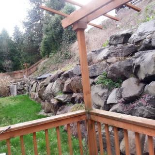A backyard view with a wooden deck and fence overlooking a rock wall and trees.