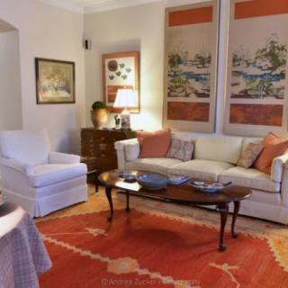 A cozy living room featuring a sofa, armchair, and a coffee table on an orange carpet, with artwork adorning the walls.