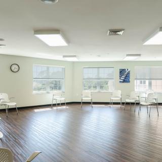 An empty room with chairs arranged along the walls, featuring large windows and a wooden floor.