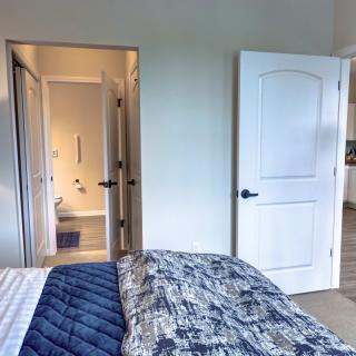 A cozy bedroom with a view into an adjacent bathroom, featuring a bed with patterned blankets and open doors.
