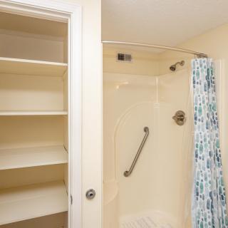 A bathroom featuring a shower with a grab bar and adjacent shelving.