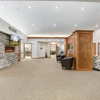 A modern waiting area featuring comfortable seating, a stone accent wall, and wood paneling, illuminated by recessed lighting.