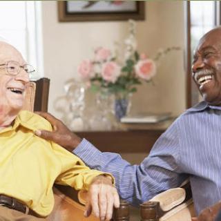 Two elderly men share a joyful moment, laughing together in a cozy indoor setting.