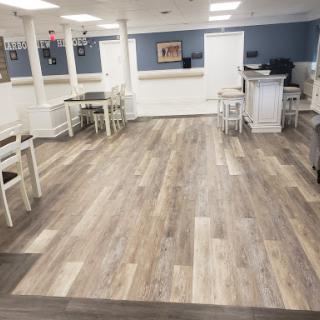 A spacious and modern dining area featuring wood-like flooring and simple white furniture.