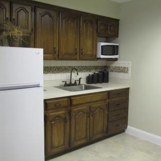 A small kitchen with wooden cabinets, a white refrigerator, microwave, sink, and countertop.