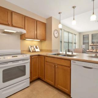 A modern kitchen with wooden cabinets, featuring a stove, dishwasher, and pendant lighting.