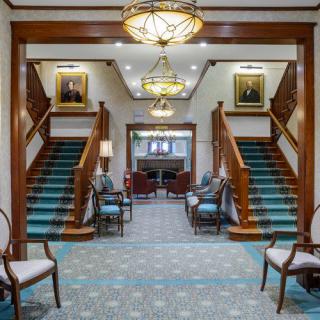A classic lobby interior featuring twin staircases, portraits, and elegant lighting.