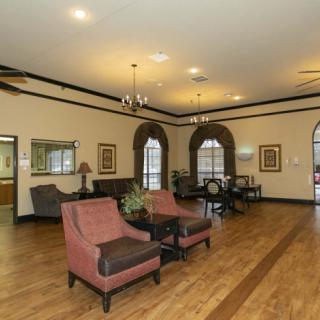 A spacious lobby with elegant furniture and chandeliers, featuring wooden flooring and large windows.
