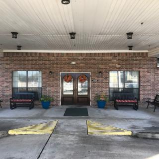 The entrance features a brick exterior with double doors, flanked by benches and potted plants.