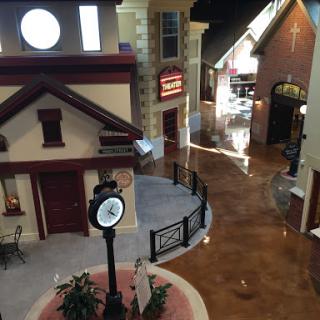 A charming indoor model village featuring a central clock and various shop facades.