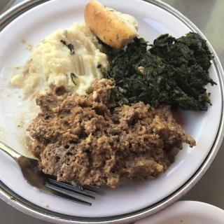 A plate featuring mashed potatoes, greens, and meat with gravy.
