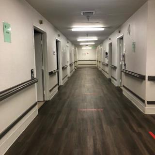 A long, well-lit hospital corridor with several doors on either side.