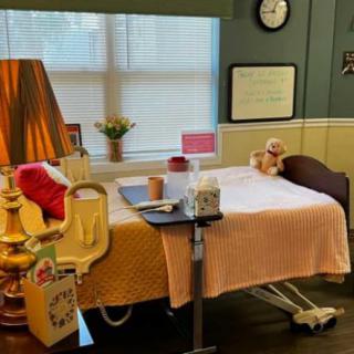 A cozy hospital room with a decorated bed, a lamp, and a teddy bear by the window.