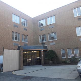 An exterior view of a brick apartment building featuring multiple windows and an entrance.