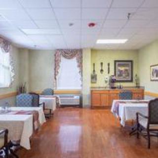 A well-lit dining area with tables and chairs, featuring decorative curtains and artwork on the walls.