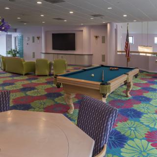 A vibrant recreation room featuring a pool table, colorful carpet, and a seating area with a television.