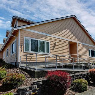 A single-story house with a ramp and well-maintained landscaping under a partly cloudy sky.