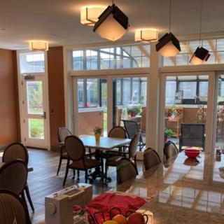 A well-lit dining area with multiple tables and chairs, surrounded by large windows and indoor plants.
