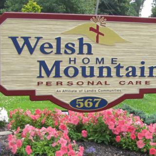 Entrance sign for Welsh Mountain Home Personal Care surrounded by flowers.