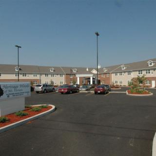 A hotel with a parking lot in front, featuring multiple cars parked and a clear sky.
