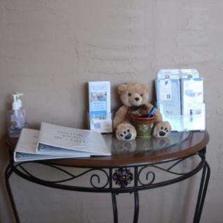 A waiting area setup with brochures, a teddy bear, and hand sanitizer on a decorative table.