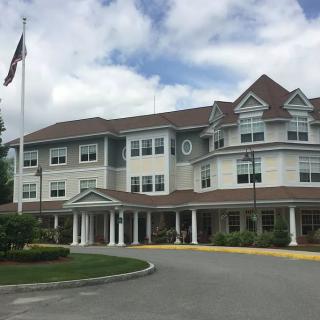 A large multi-story building with an American flag, featuring a grand entrance and landscaped grounds under a cloudy sky.