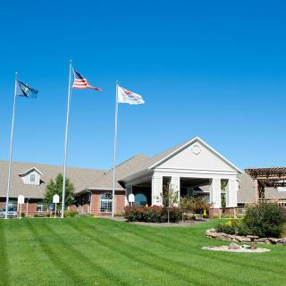 A view of a building with three flags in front, surrounded by green lawn under a clear blue sky.