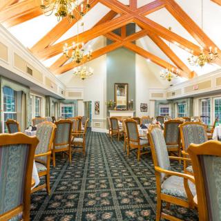An elegant dining room with wooden beams, chandeliers, and neatly arranged tables and chairs.