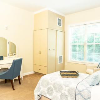 A bright bedroom featuring a vanity table with a chair, large wardrobe, and natural light from the window.