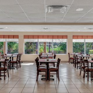 An empty dining area with neatly arranged tables and chairs, featuring large windows.