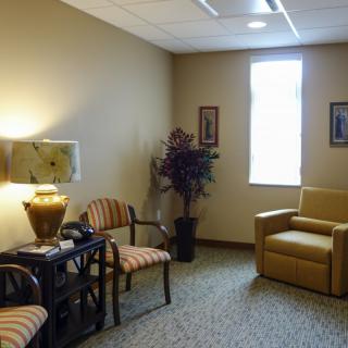 A cozy waiting room with comfortable chairs, a lamp, potted plant, and wall art.