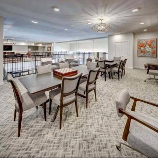 A spacious and modern lounge area featuring dining tables with chairs, accented by a patterned carpet and contemporary lighting.