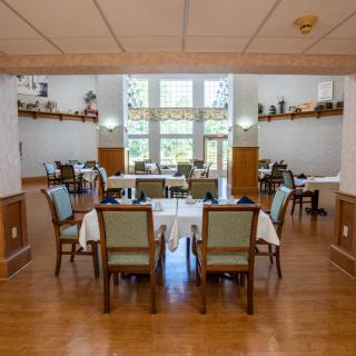 A spacious dining room featuring neatly arranged tables and chairs, with large windows providing ample natural light and decorative shelves enhancing the ambiance.
