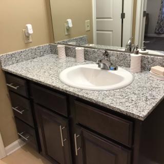 A bathroom with a granite countertop and sink, featuring dark wood cabinets and a mirror.