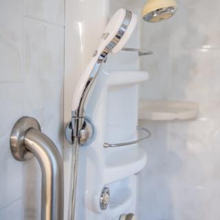 A modern bathroom shower setup featuring a handheld showerhead, grab bar, wall shelf, and tiled wall.